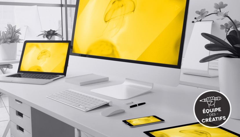 Bureau blanc avec ordinateur, portable, tablette et téléphone affichant une image jaune de méduse.