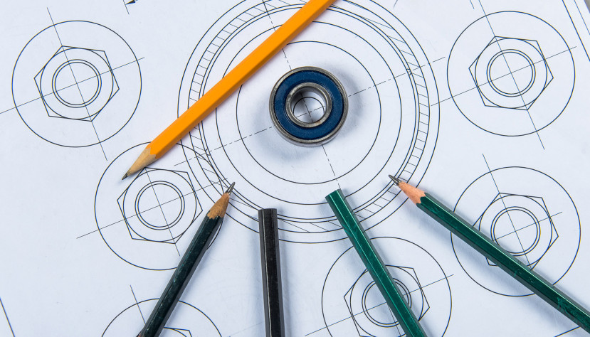 Roulement à billes posé sur un dessin industriel avec plusieurs crayons de couleur autour.