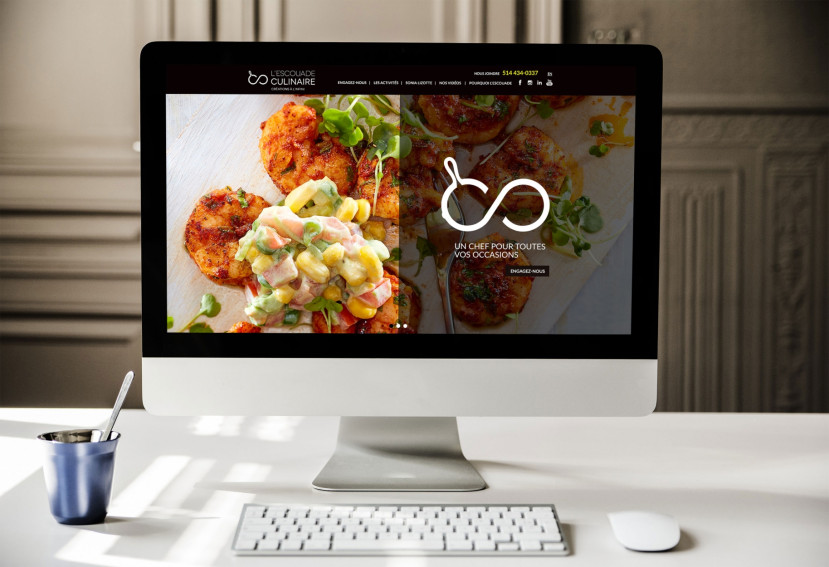 Ordinateur sur un bureau en bois avec le site web de l'Escouade Culinaire, lampe blanche, plante en pot et chaise blanche.