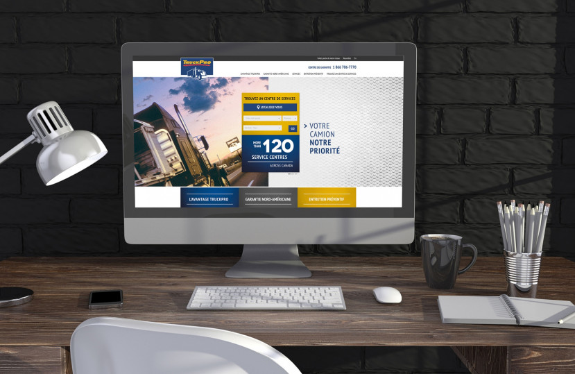 Écran d'ordinateur affichant le site TruckPro avec options de recherche de centres de service et image de camion sur un bureau en bois.