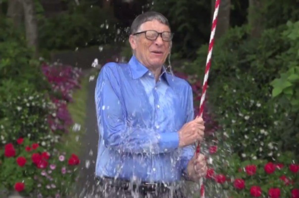 Homme en chemise bleue éclaboussé d'eau en tenant une corde rouge et blanche dans un jardin fleuri.