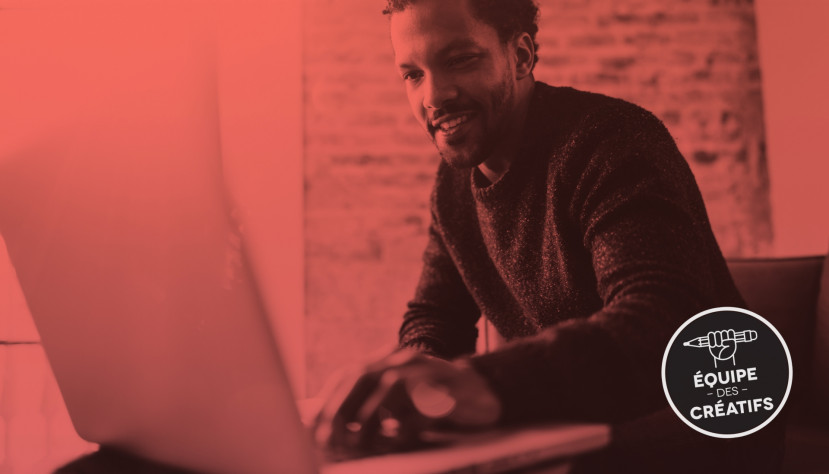 Homme souriant travaillant sur un ordinateur portable dans un espace avec mur en briques et filtre rouge.