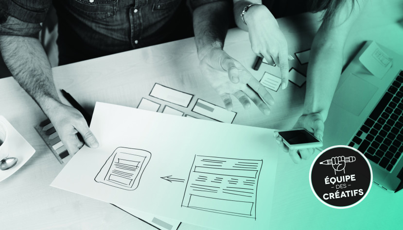 Deux personnes collaborent sur des croquis de site web avec un ordinateur portable et un téléphone sur la table.